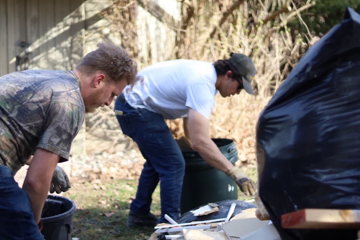 Two crew members loading junk into bins in a backyard