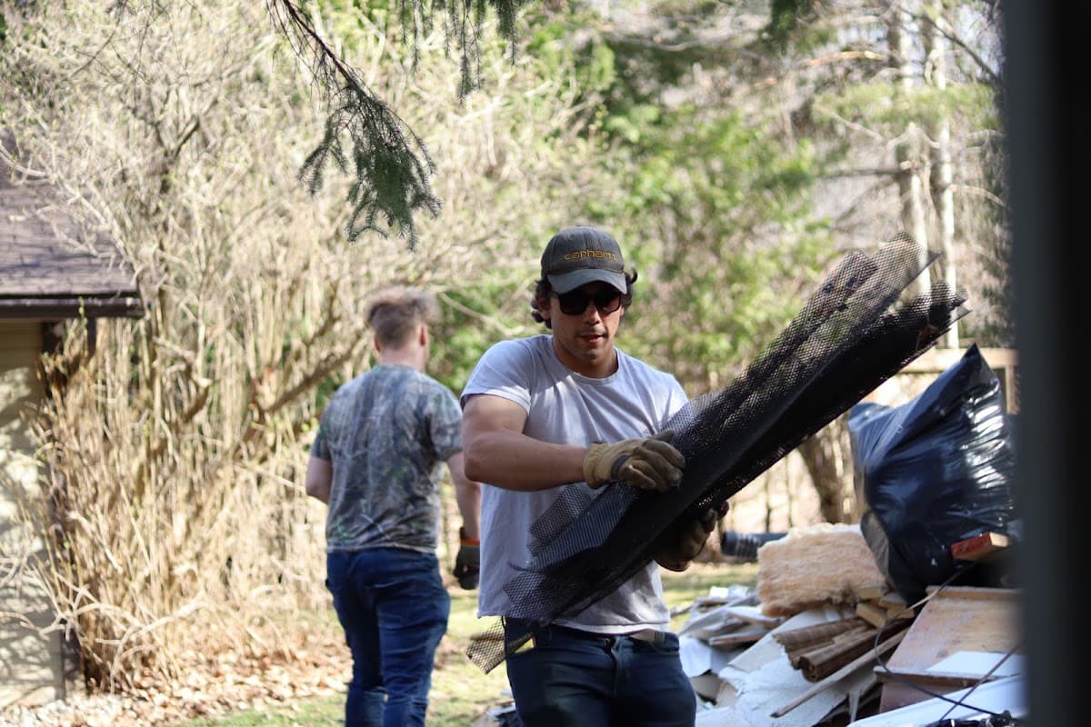 Crew member carrying mesh sheeting away from a renovation debris pile